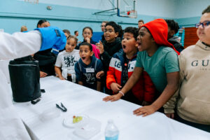 SPARK 2024. Arian Jadbabaie (in the lab coat), a postdoc in the Doyle group, demonstrates flux pinning in a YBCO superconductor to students at UP Academy Dorchester.